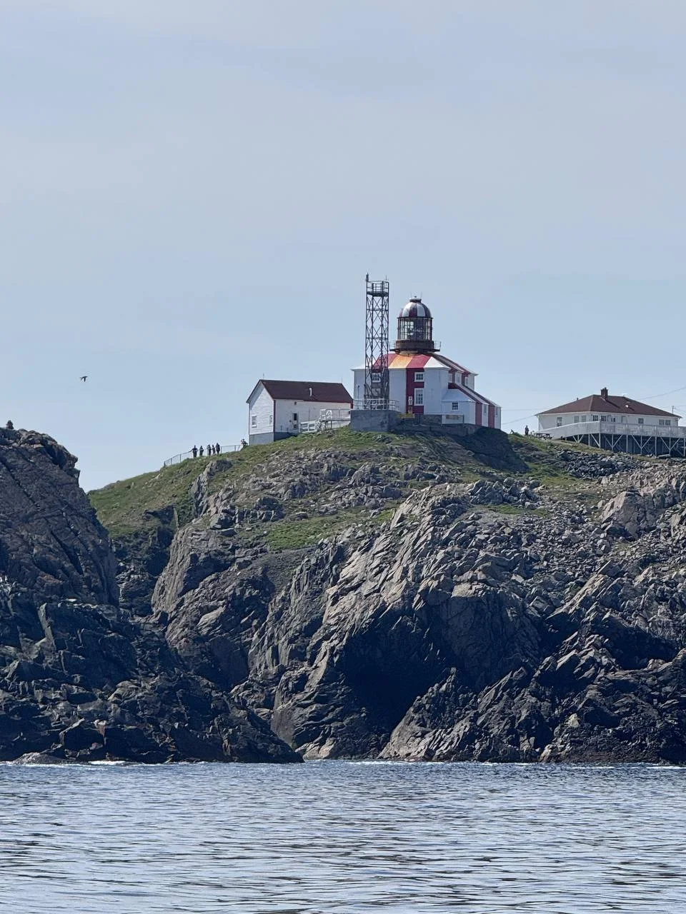 Lighthouse complex above steep rocky Atlantic cliffs photographed from the water